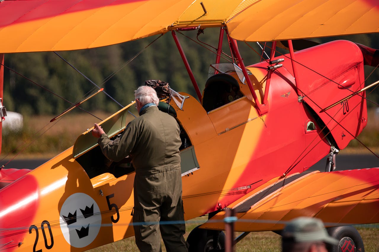 Mechanic in uniform performing inspection on a colorful vintage biplane outdoors.
