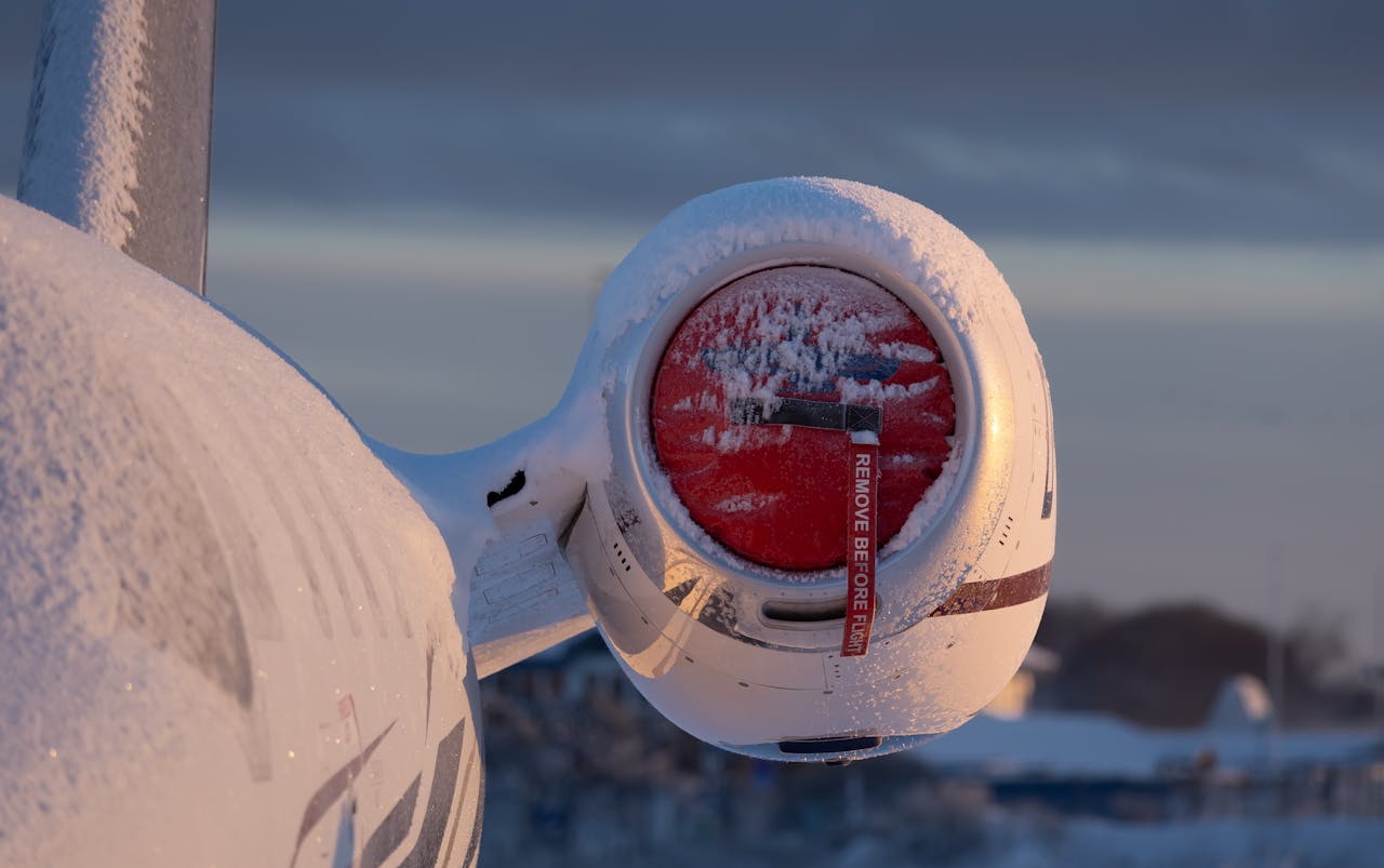 Airplane engine covered in snow at sunrise, showcasing winter aviation scene. Remove Before Flight tag visible.